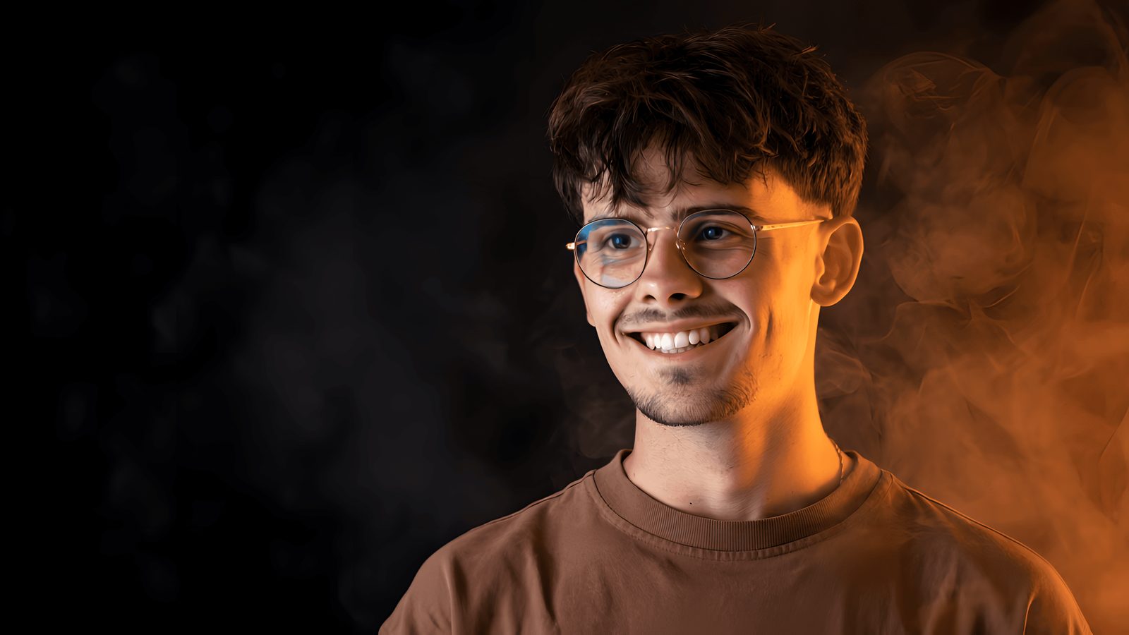 Portrait of Anthony Durand, smiling, lit in warm orange against a dark background
